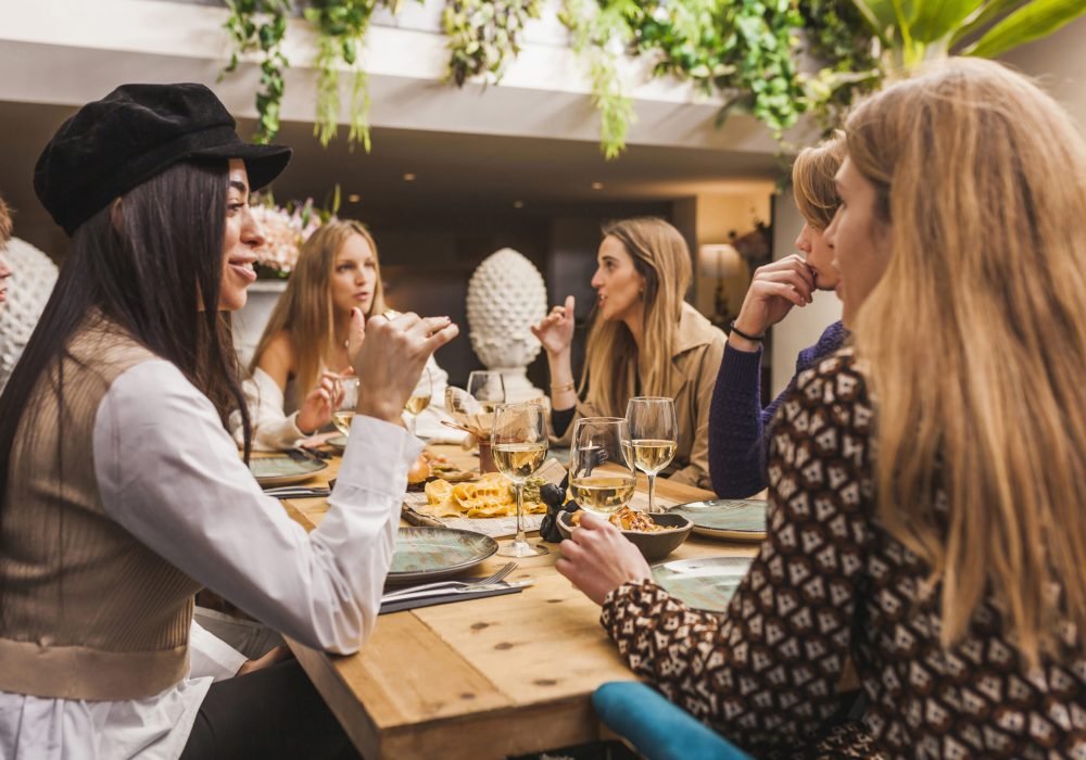 Group of young caucassian people sitting at dinner table and having friendly conversation at restaurant. Millennial friends enjoying together, eating and drinking alcohol. friendly lifestyle concept.